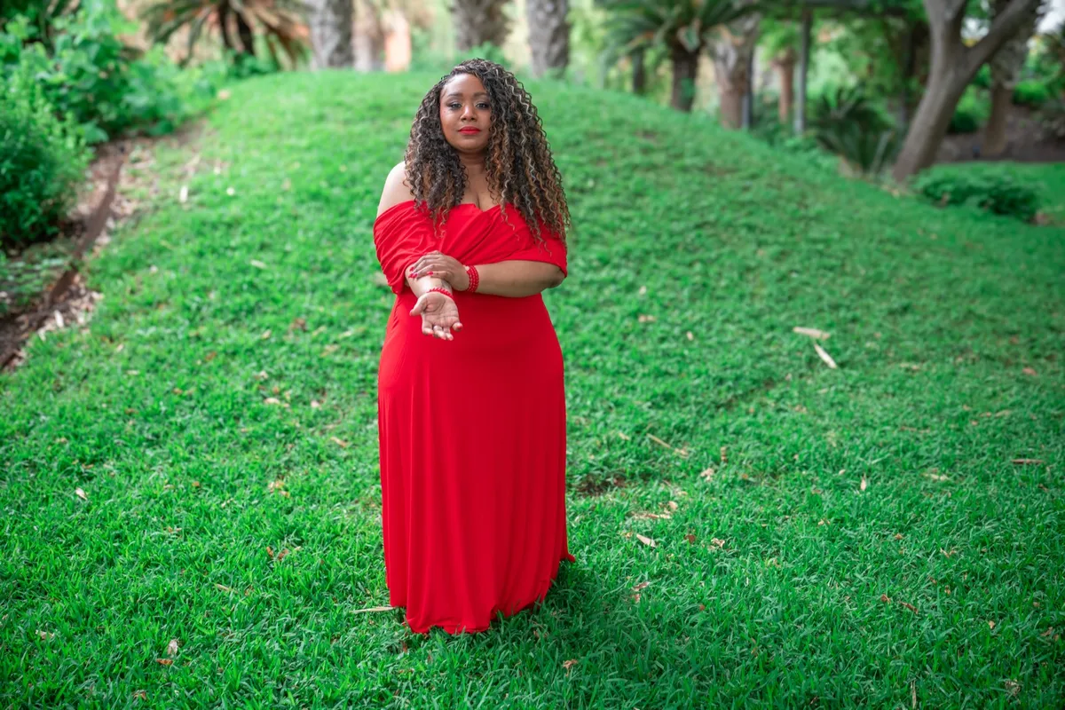 Andrea “Vocab” Sanderson standing on a grassy hill among palm trees, wearing a red gown